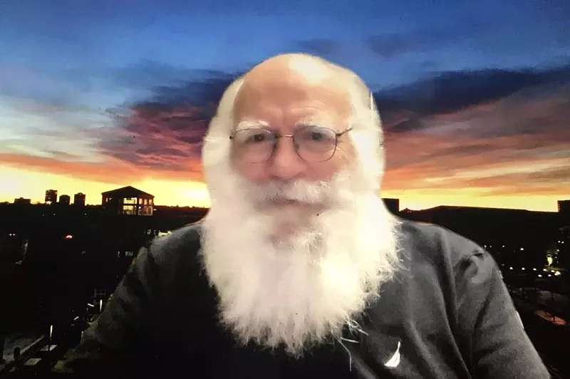 Image: John Wren sitting in front of a sunset background.