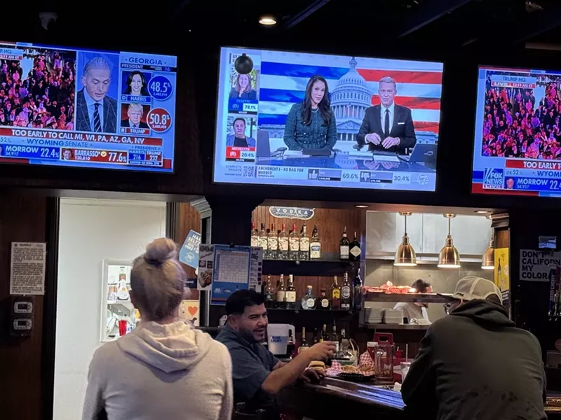 Image: A woman watches TV at a bar.