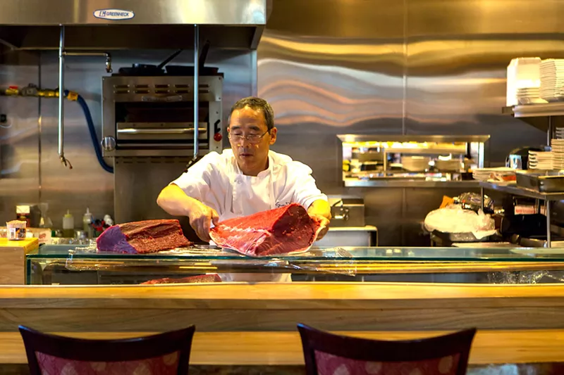 Image: a man in a chef's coat holding a large piece of raw tuna