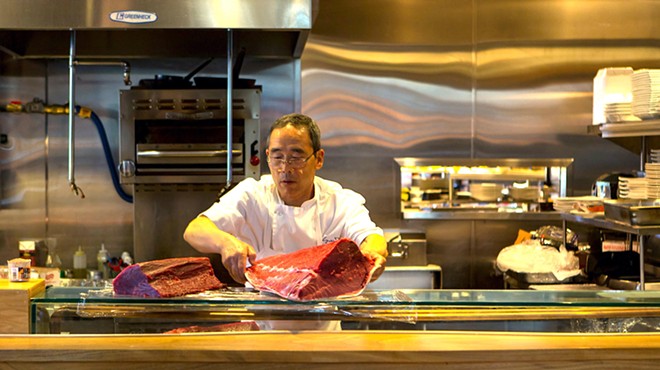 a man in a chef's coat holding a large piece of raw tuna